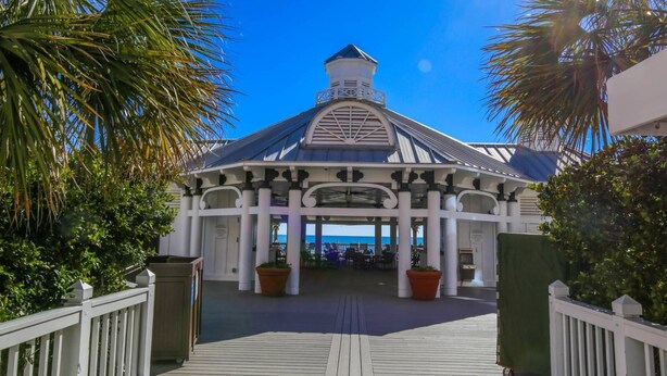 A covered outdoor area with a white roof and columns, surrounded by palm trees and a wooden deck.