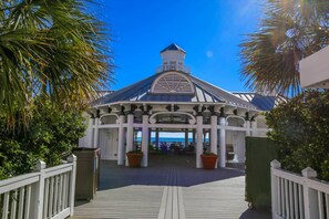 A covered outdoor area with a white roof and columns, surrounded by palm trees and a wooden deck.