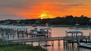 A waterfront marina with docked boats, a pier with a gazebo, and a sunset in the background.