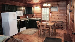 A cabin-style kitchen with wooden cabinets, a refrigerator, microwave, and a dining table with chairs.