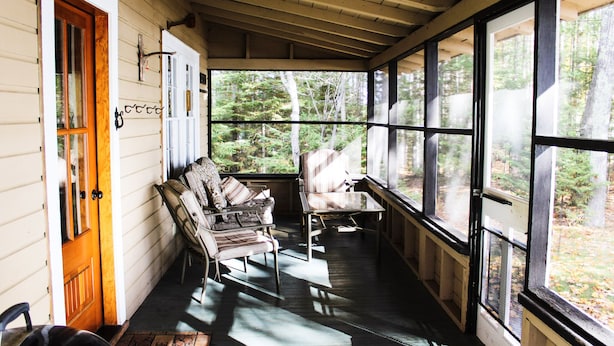 A covered porch with wooden benches and a table, large windows with a forest view, and a door with a wooden frame.