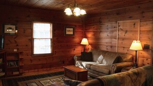 A cozy cabin-style room with wooden walls, a leather sofa, a small wooden table, and two lamps.