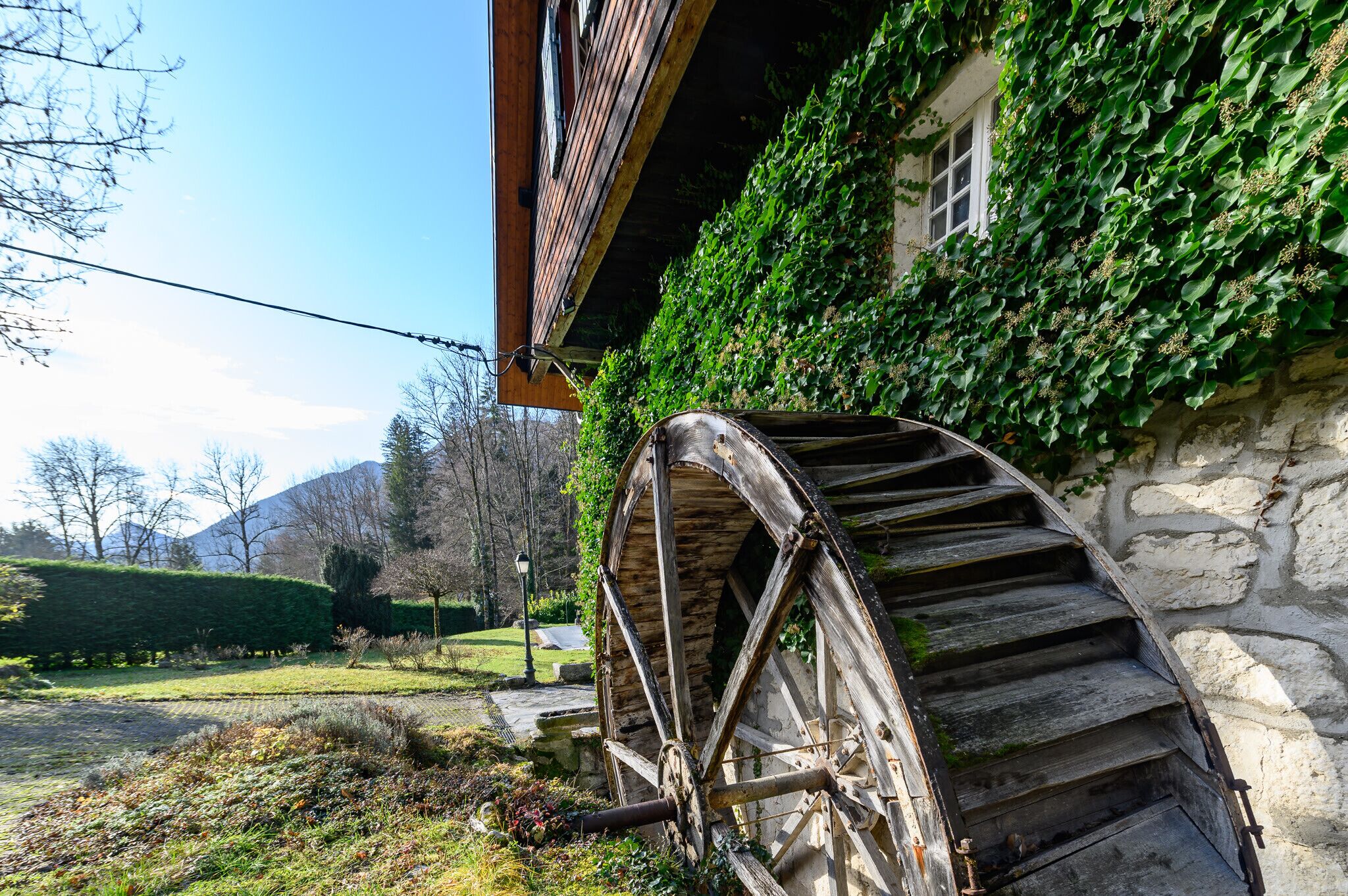 Un bâtiment rustique en pierre, agrémenté d’une grande roue à eau en bois fixée sur le côté.
