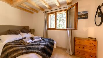Une chambre à coucher avec une tête de lit en bois, une grande fenêtre avec des rideaux, une commode en bois et un tableau accroché au mur.