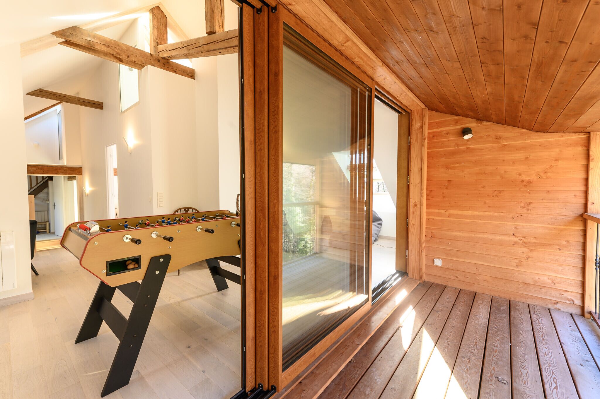 Une pièce au plancher de bois, équipée d’un baby-foot et d’une porte-fenêtre coulissante donnant sur un espace extérieur.