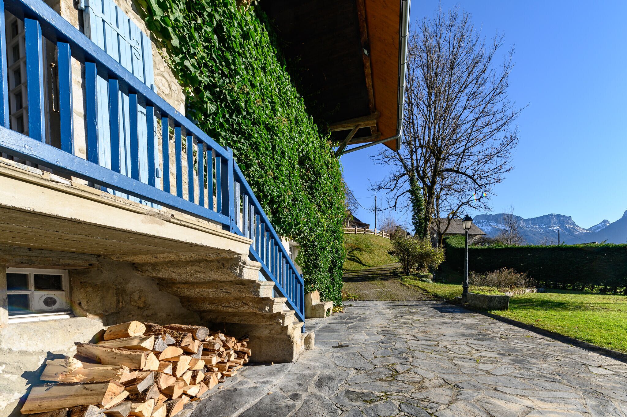 A stone pathway leading to a building with a blue railing and a stack of firewood.