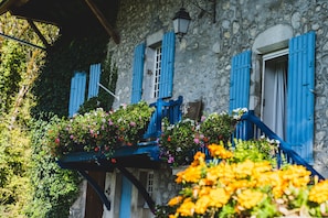 Un edificio de piedra con contraventanas azules y un balcón lleno de flores.