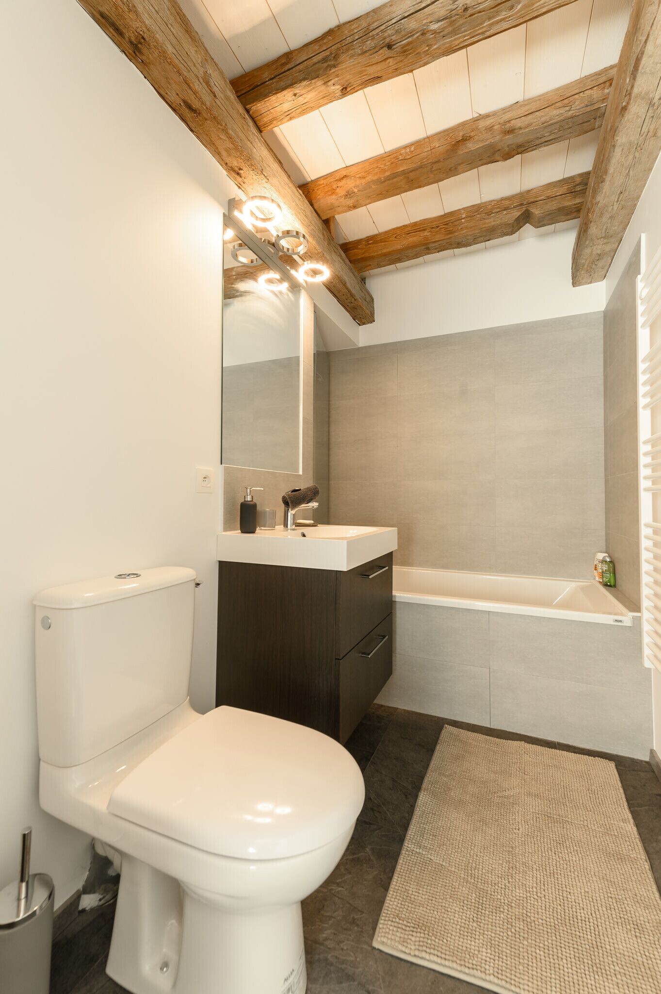Een moderne badkamer met een wit toilet, een donker houten wastafelmeubel en een bad.