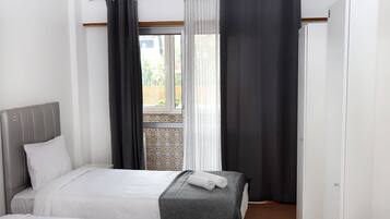 A bedroom with two beds, a window with curtains, and a view of the outside.