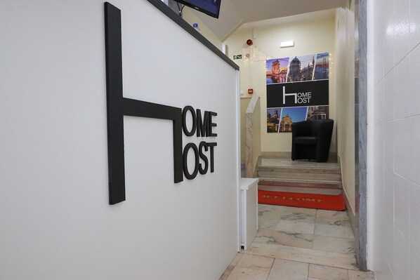 Un pasillo con un letrero que dice 'ONE HOME HOST', una escalera y un tapete de bienvenida.