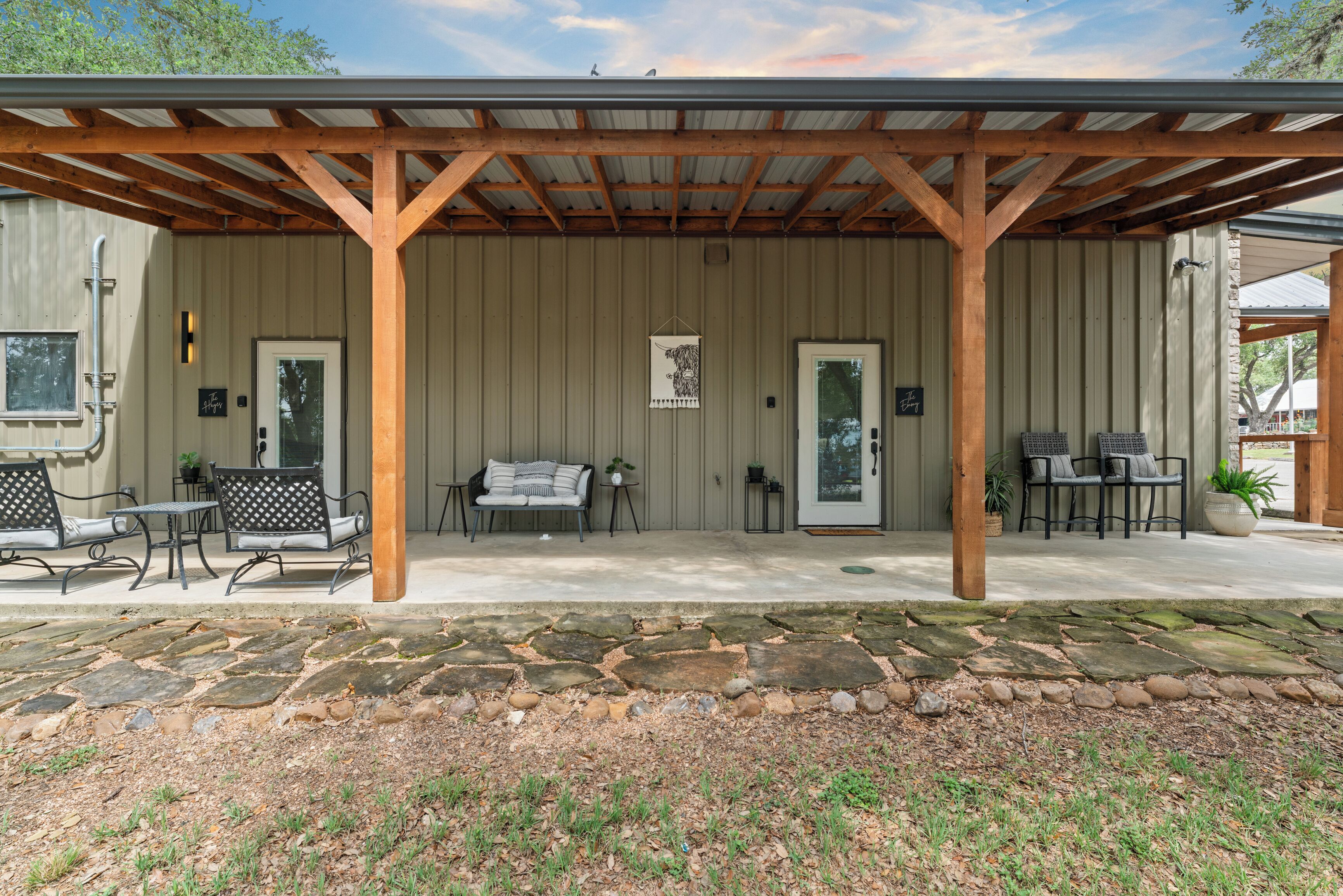 A covered patio with stone flooring, wooden beams, and outdoor seating.