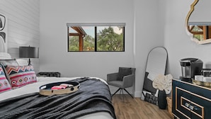 Une chambre moderne avec un lit, une chaise, une commode et une fenêtre donnant sur des arbres.
