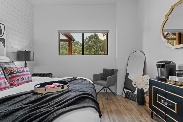 Un dormitorio moderno con cama, una silla, cómoda y ventana con vistas a árboles.