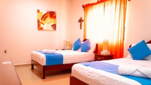 A hotel room with two beds, each with blue and white bedding, a wooden nightstand, a wall-mounted cross, and a painting on the wall. - Hotel Bacalar Magico (Bacalar)