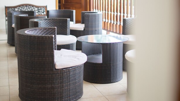 A covered outdoor seating area with wicker furniture and a glass table, featuring a wooden door and a view of greenery. - Hotel Bacalar Magico (Bacalar)