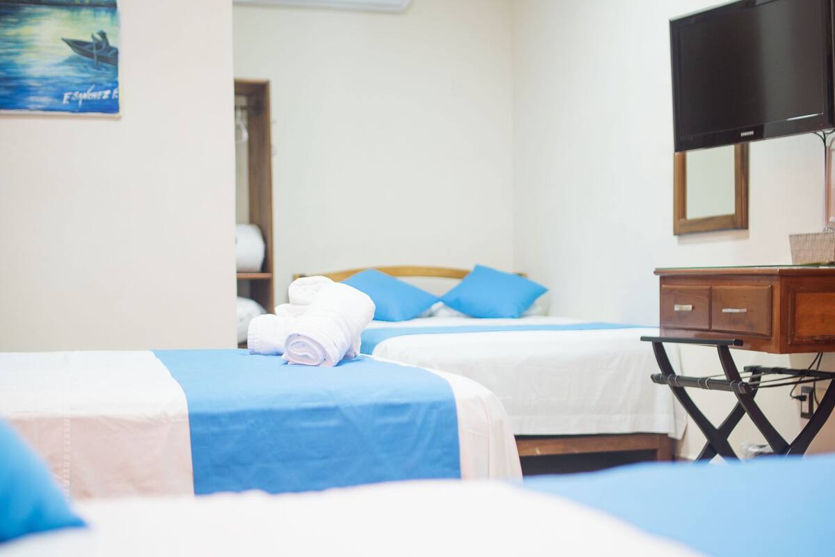 A hotel room with two beds, a TV, a desk, and an air conditioning unit.