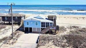 A beach house with a staircase leading to a deck, a beach view, and a sandy area with sparse vegetation. - OCEANFRONT, Ocean Views, Screened porch, KH17, Down by the Sea (Kitty Hawk)