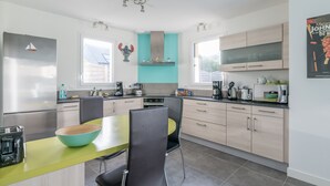 A modern kitchen with a central island, light wood cabinets, and a teal accent wall.