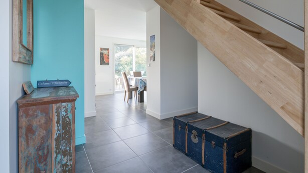 A staircase with wooden railings and a blue wall. There is a rustic cabinet and a vintage suitcase on the floor.