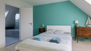 A bedroom with a white bed, teal walls, a wooden nightstand, and a view of a balcony.