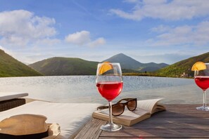 A wooden table with a book, a pair of sunglasses, and two glasses of red wine with orange slices on a lakeside view. - VILLA AMANTA - Nine Bedroom Villa, Sleeps 16 (Perugia)