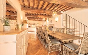 A spacious dining area with a long wooden table and wicker chairs, a kitchen in the background, and a staircase with a metal railing. - VILLA AMANTA - Nine Bedroom Villa, Sleeps 16 (Perugia)