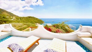 Un espace piscine aménagé sur le toit, avec des chaises longues et une vue sur la mer et les collines.