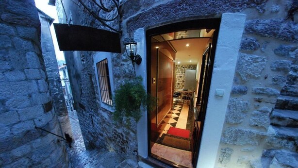 A narrow stone corridor with a wooden door leading into a room with a checkered floor and a red carpet. - Apartment with 2 bedrooms with hot tub and water bed (Kotor)