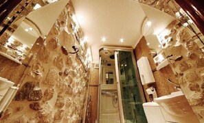 Bathroom features a glass-enclosed shower, white sink, and mirror, set against a natural stone wall design.