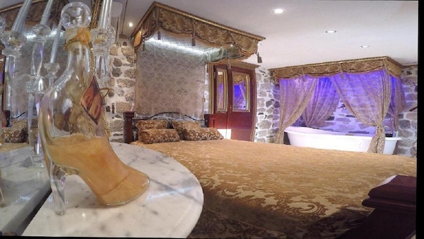 A bedroom with a large bed, stone walls, and a canopy bed with purple curtains.