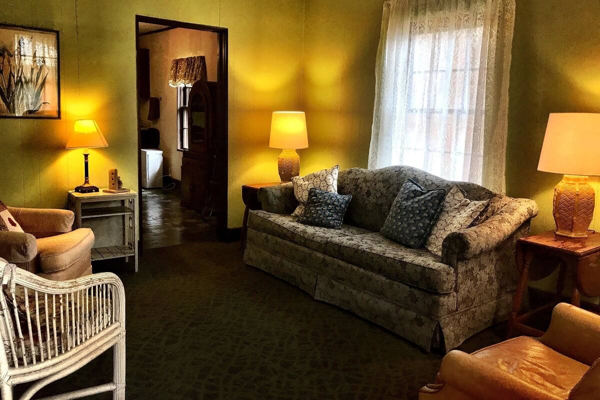 A cozy living room with a sofa, two armchairs, and a small table. A doorway leads to another room.