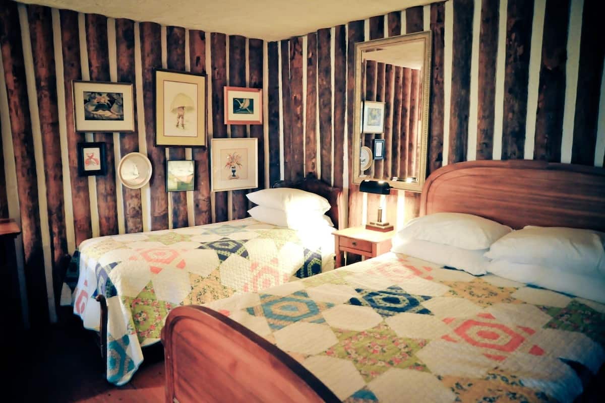 A room with two beds, wooden walls, and several framed pictures on the wall.