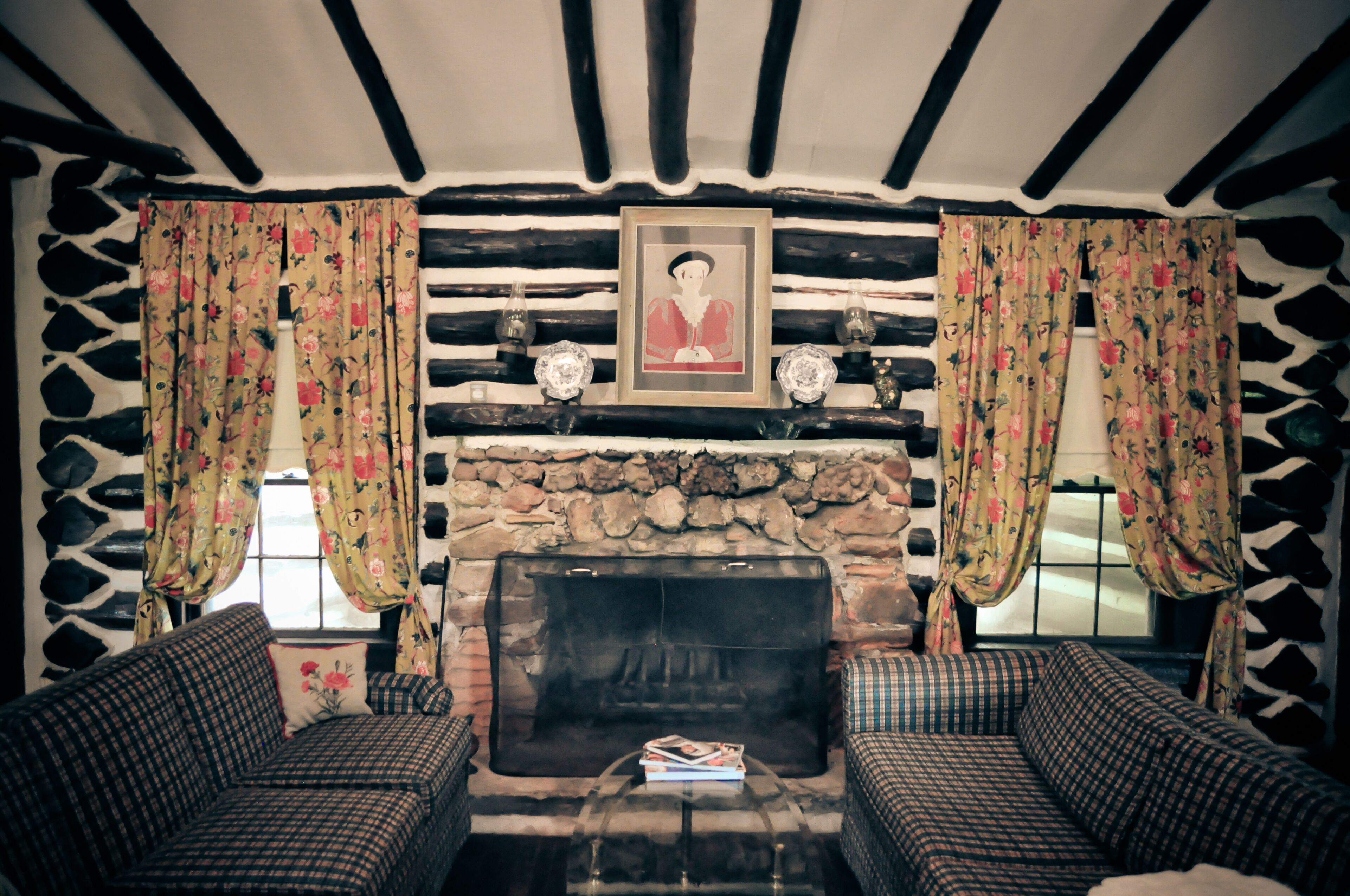 Una sala de estar acogedora con chimenea de piedra, dos sofás a cuadros y cortinas con motivos florales.