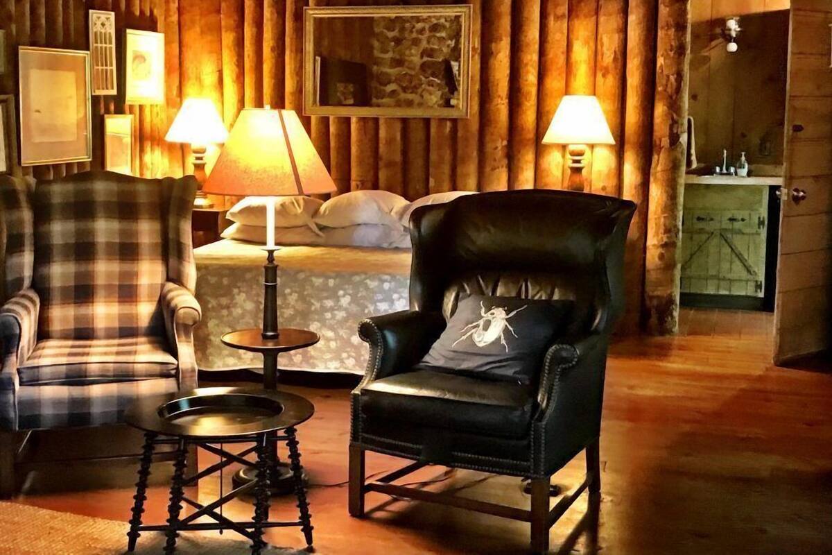 A cozy room with a bed, two chairs, a small table, and two lamps.