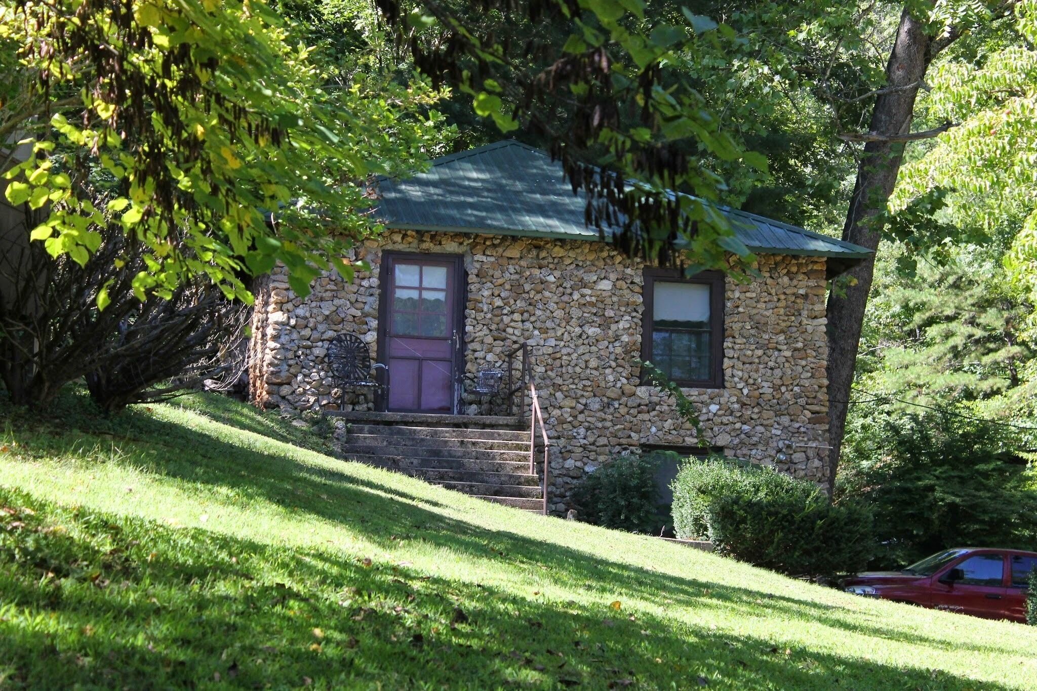 A stone house with a green roof, a purple door, and a small porch with steps.