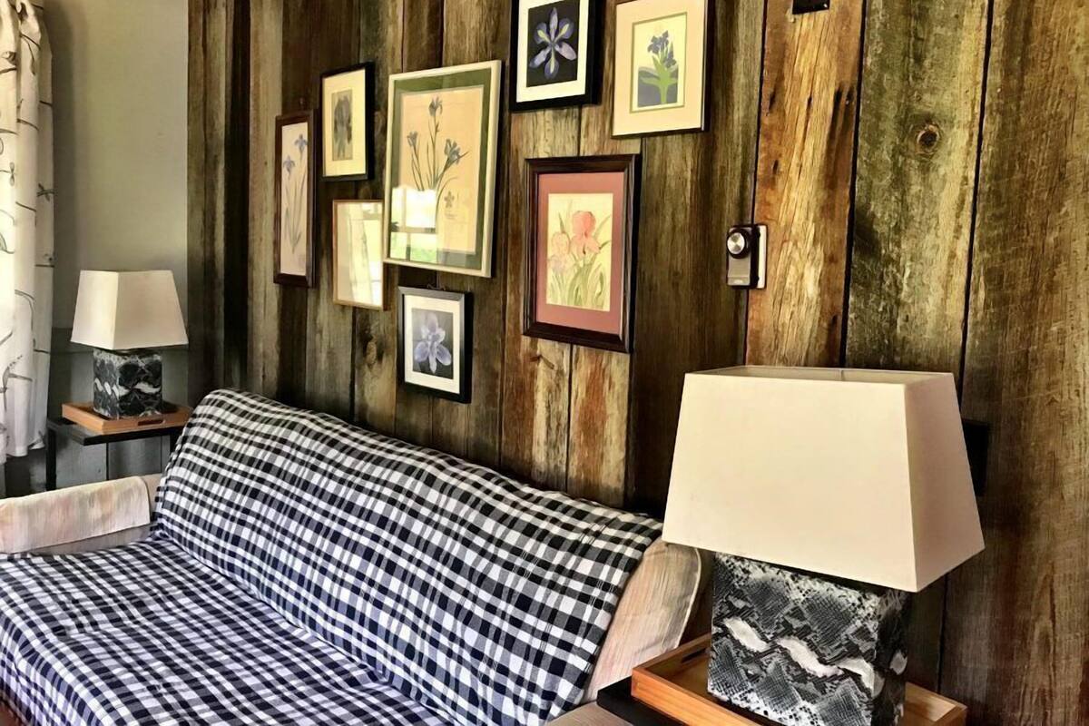 A room with a wooden wall, a checkered sofa, and multiple framed pictures.