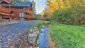 A wooden lodge with a stone pathway leading to the entrance, surrounded by autumn foliage. - Smokey Max Cabin sleeps 8, hot tub, jacuzzi , pool table (Pigeon Forge)