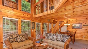 A cozy cabin interior with a wooden staircase, a sofa set, and a dining area. - Smokey Max Cabin sleeps 8, hot tub, jacuzzi , pool table (Pigeon Forge)