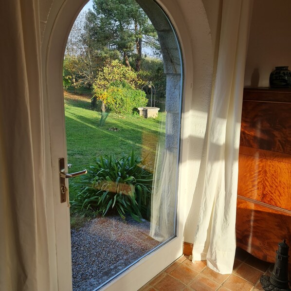 A doorway leading to a garden with a lawn, a small tree, and a bench.