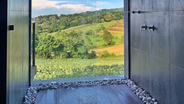Un baño moderno con un ventanal grande, un cabezal de ducha y vistas a un paisaje verde.