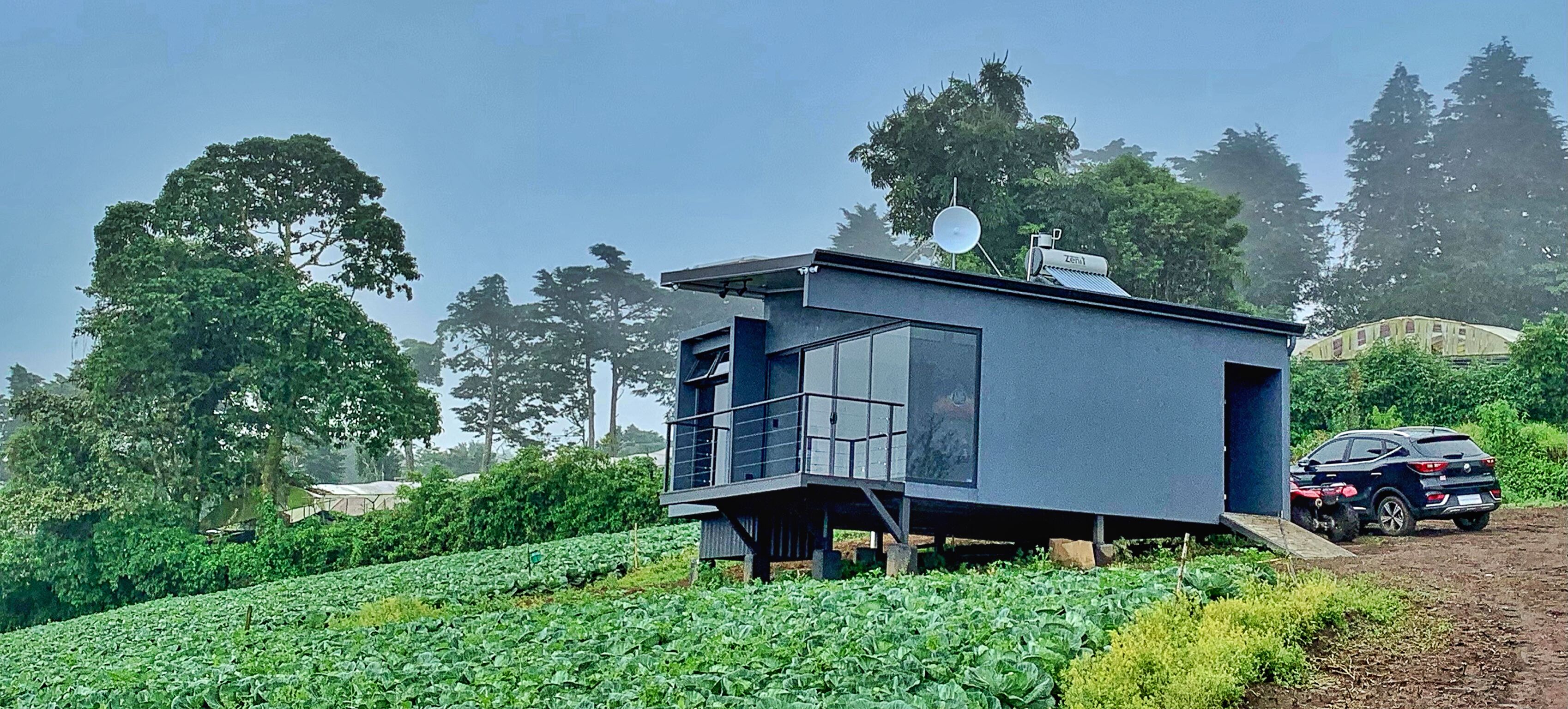 Un edificio moderno de una sola planta con balcón, ubicado en un campo verde exuberante con un automóvil cerca.