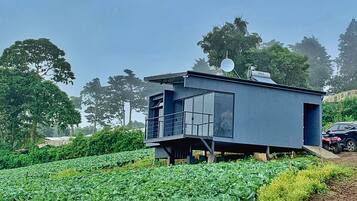 Un edificio moderno de una sola planta con balcón, ubicado en un campo verde exuberante con un automóvil cerca.