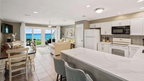 A modern kitchen with white cabinets, a central island, and a view of the ocean. - Blue Tide (Panama City Beach)