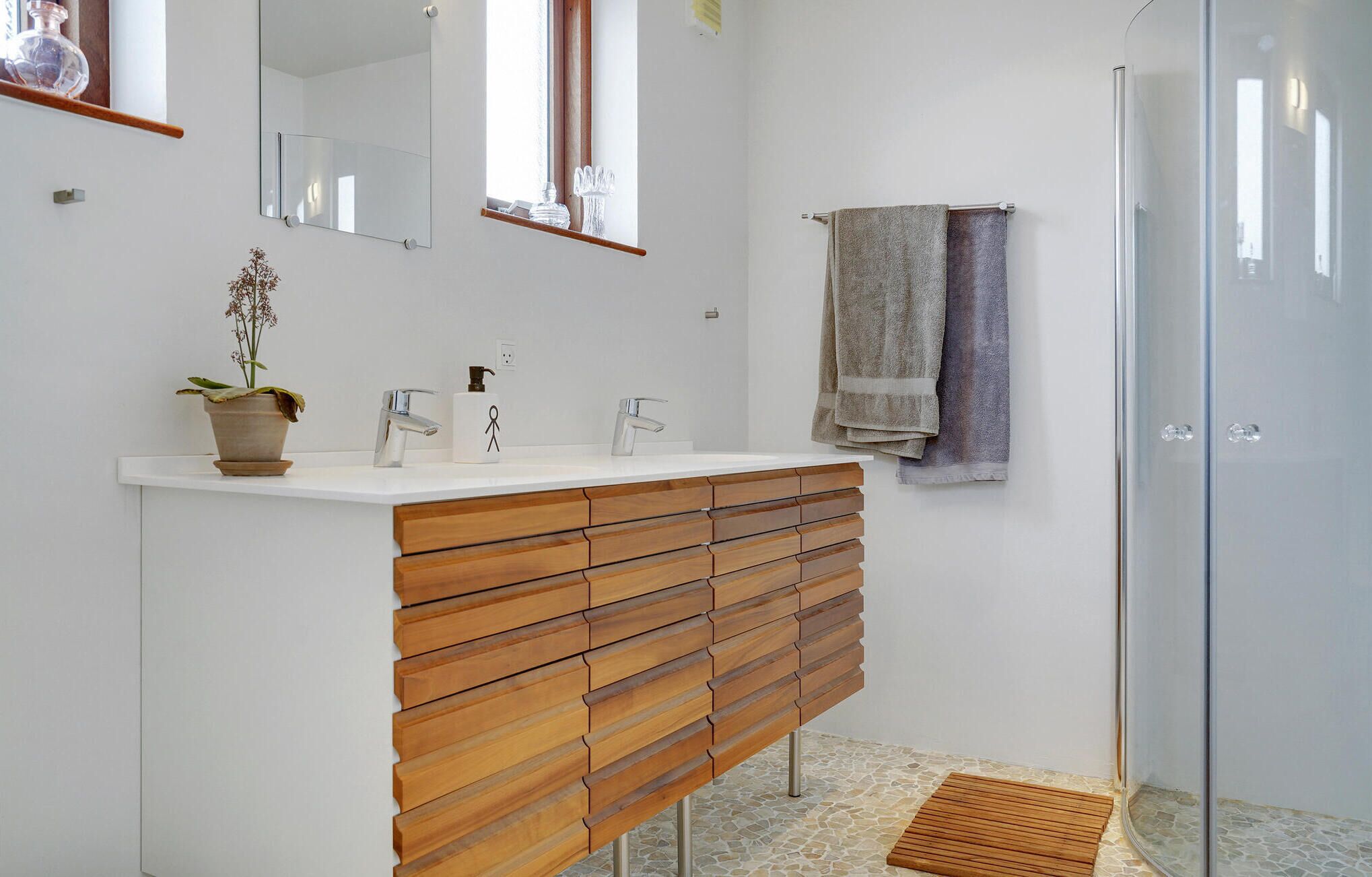 Un baño moderno con tocador de madera, cabina de ducha de vidrio y una planta en maceta.