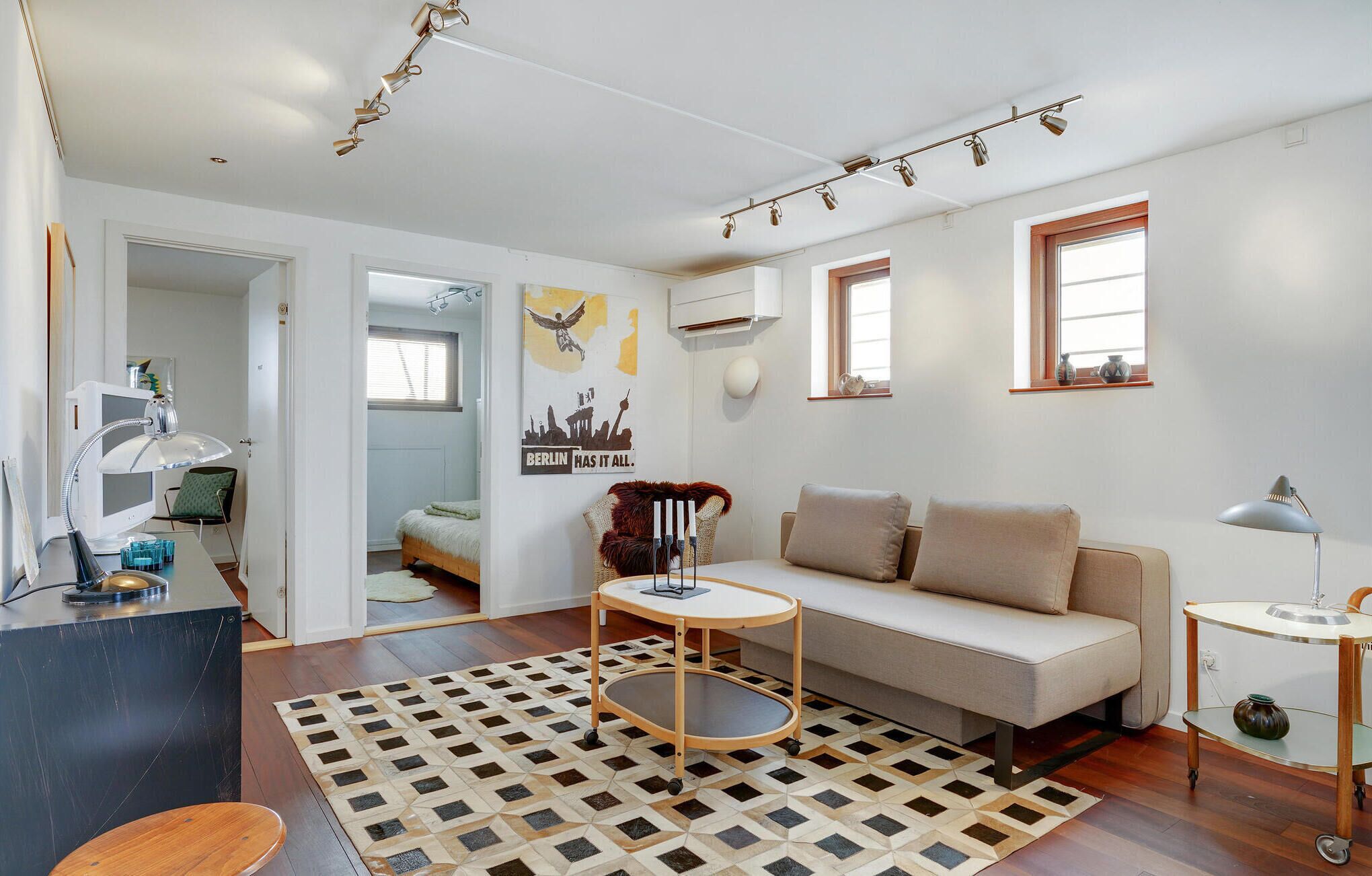 A modern living room with a sofa, a small round table, a desk with a lamp, and a patterned rug.