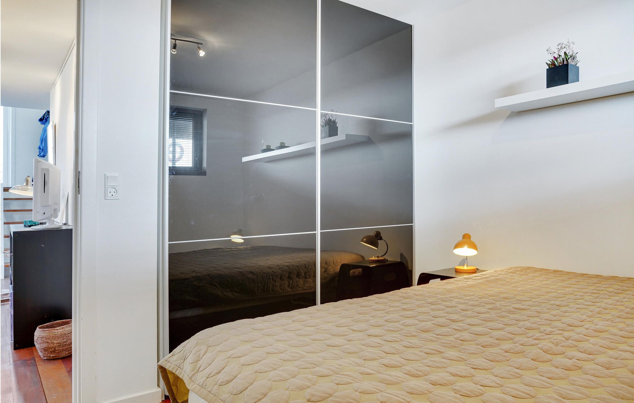 A bedroom with a bed, bedside table, lamp, and a wardrobe with a mirror.