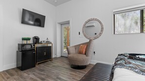 A modern bedroom with a bed, a round mirror, a television, a microwave, and a small kitchenette. - The Hayes (Bulverde)