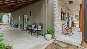 A covered patio area with outdoor seating, a stone wall, and a wooden ceiling. - The Hayes (Bulverde)