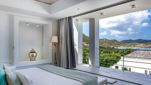 Une chambre moderne avec un grand lit, une table de chevet, une lampe et une vue sur un paysage côtier.