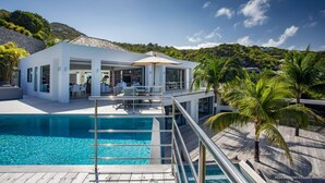 Une villa moderne dotée d’une piscine, d’un espace extérieur aménagé et offrant une vue sur une colline verdoyante.
